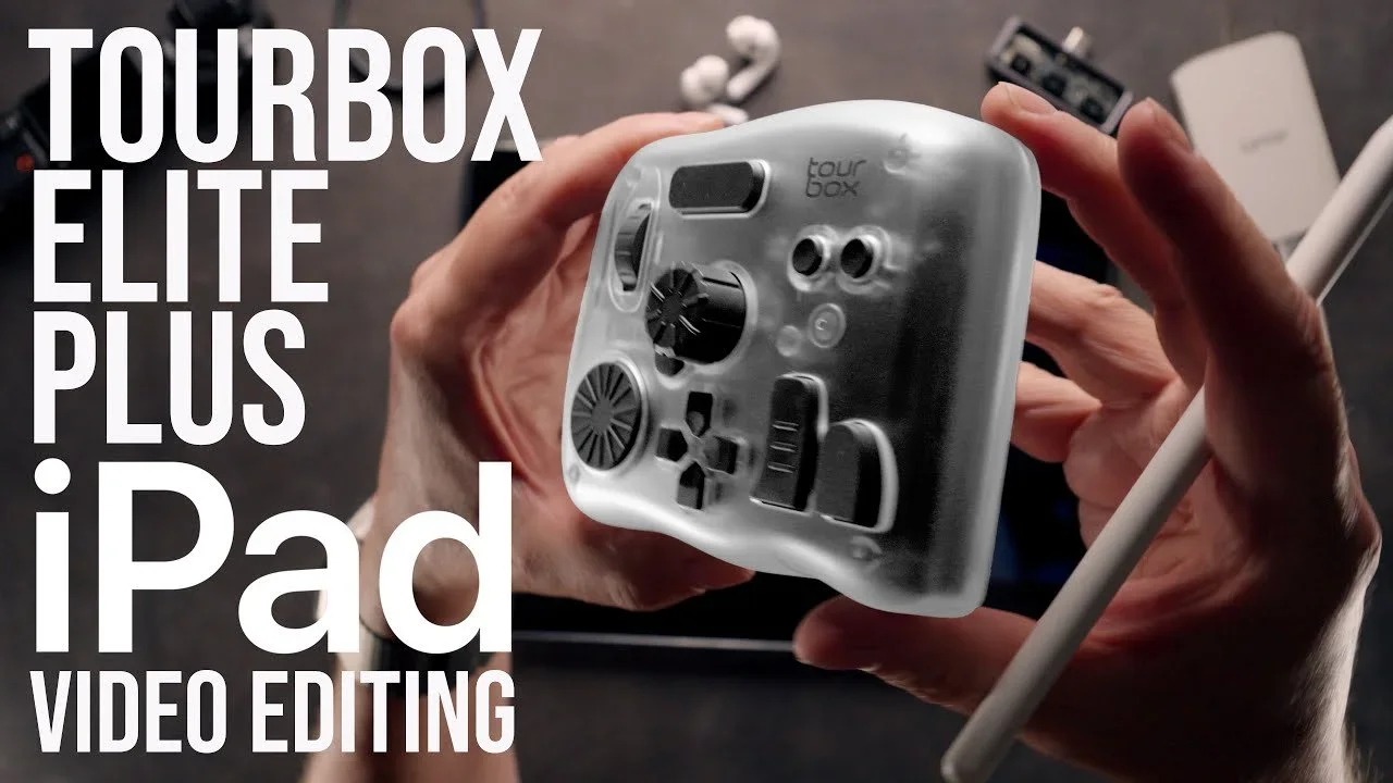 Close-up of a hand holding a TourBox Elite Plus creative controller with an iPad, used for video editing, on a dark table with other electronic accessories around.