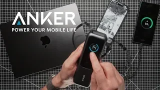 Hand holding a portable charger connected to a smartphone and a wireless earbud case, with an Anker product box and a laptop in the background.