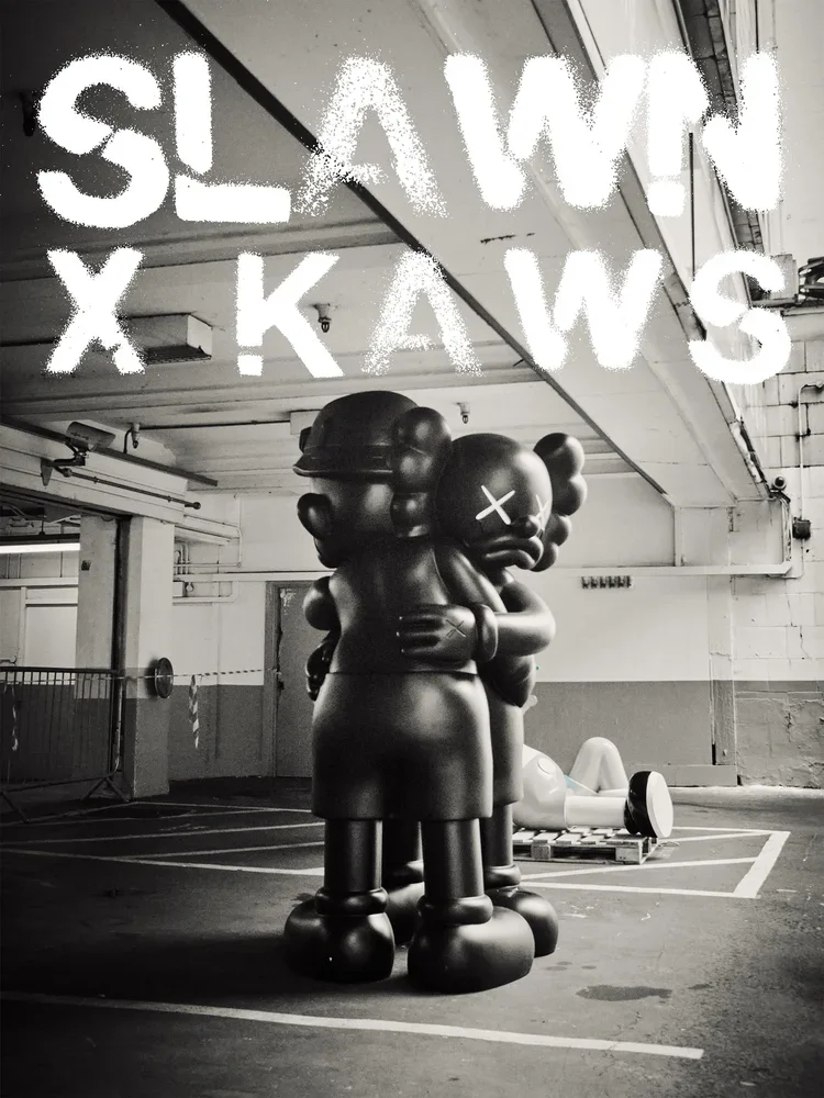Black and white photo of a large, stylized sculpture of figurines hugging in a parking garage, with graffiti-style text overlay reading 'SLAM X KAWS'.