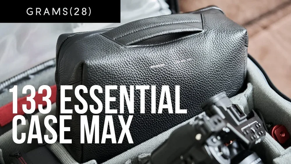 Close-up of a black camera bag inside a gray carrying case, with a black camera and a black hard case in the background, and text overlay reading "133 Essential Case Max".