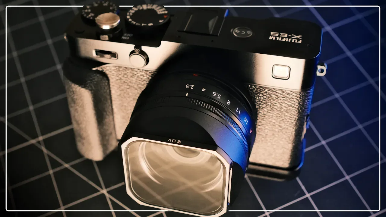 A Fujifilm X-E5 mirrorless camera with a lens attached, placed on a grid-patterned surface.