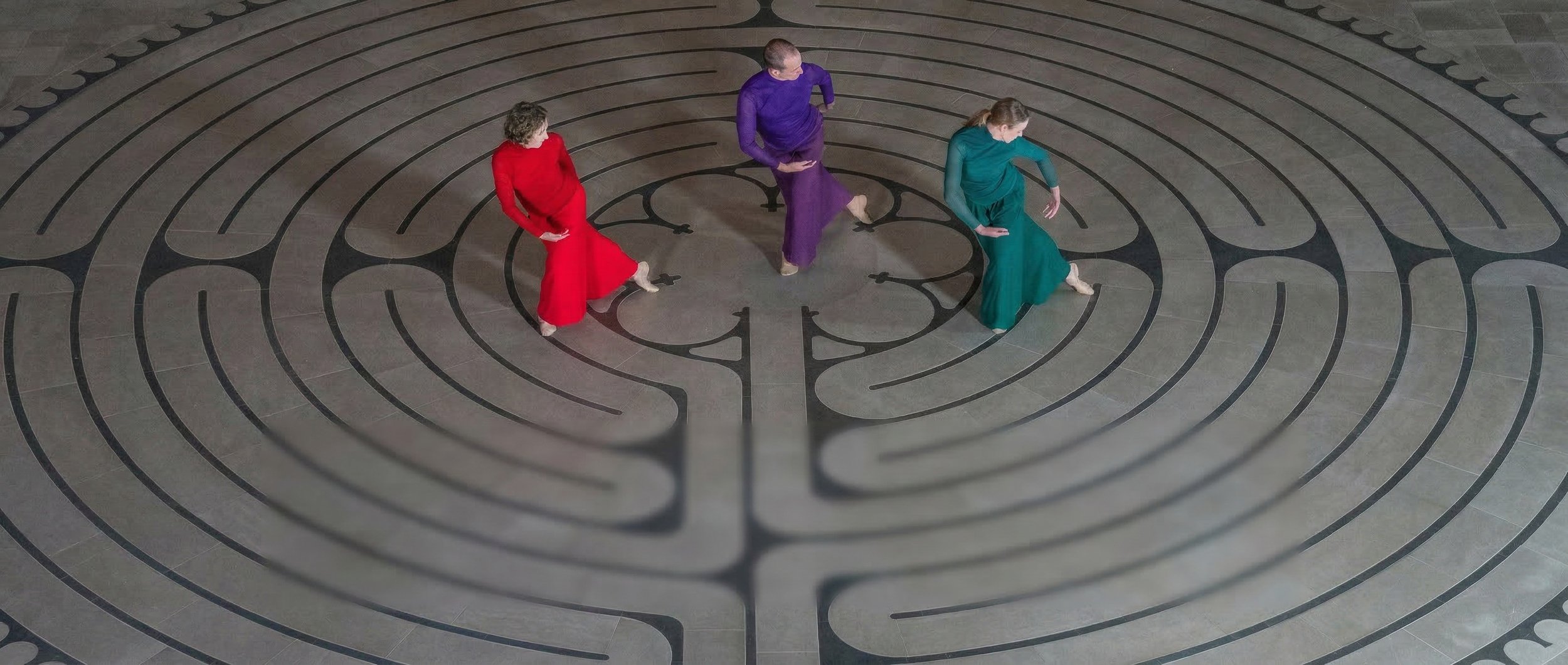 Three dancers in jewel tones create the same shape on a floor with a labyrinth pattern