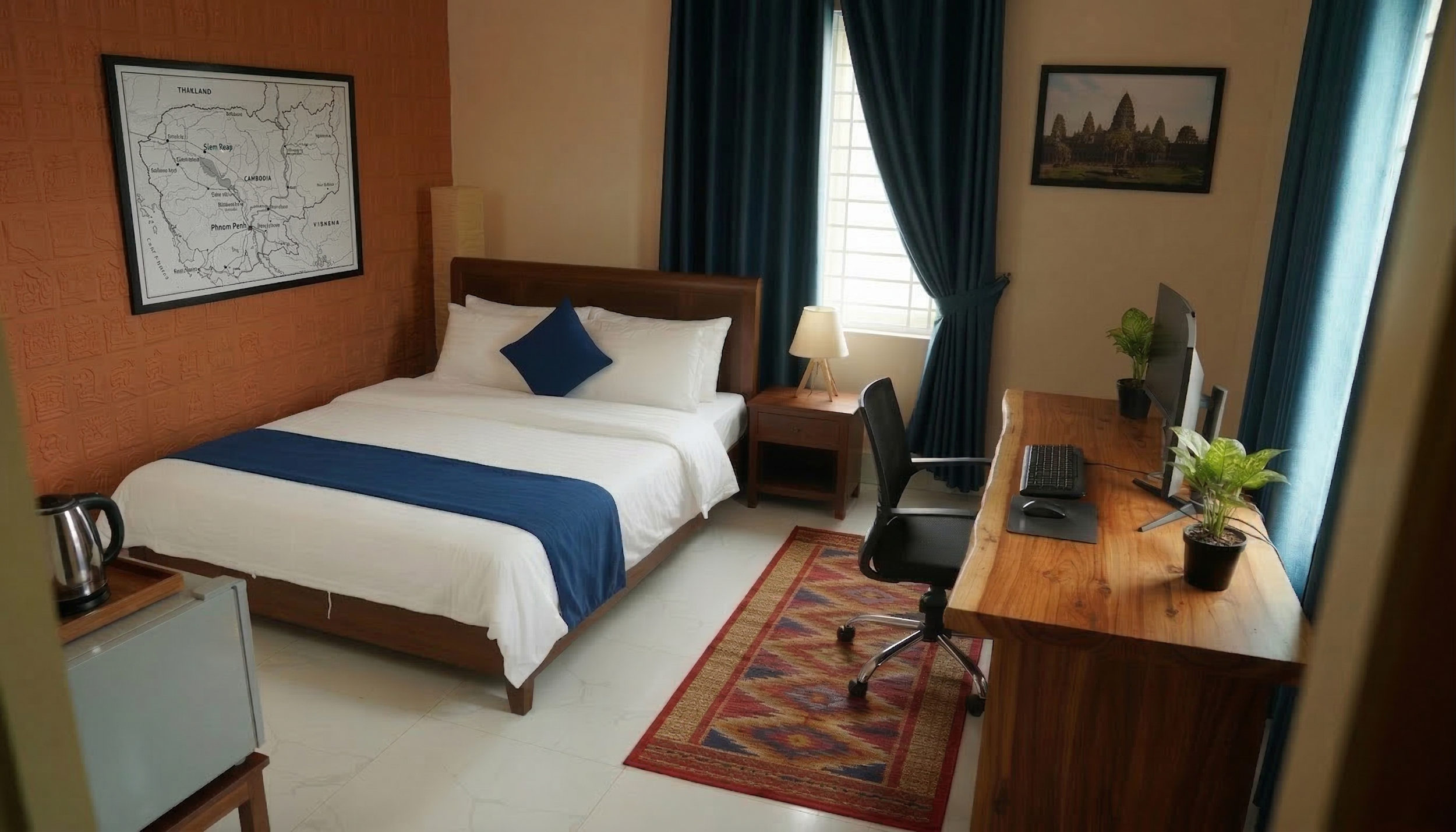 A hotel room with a double bed, a wooden desk with a flat-screen monitor, and potted plants, with a window covered by dark blue curtains and decorative artwork on the walls.