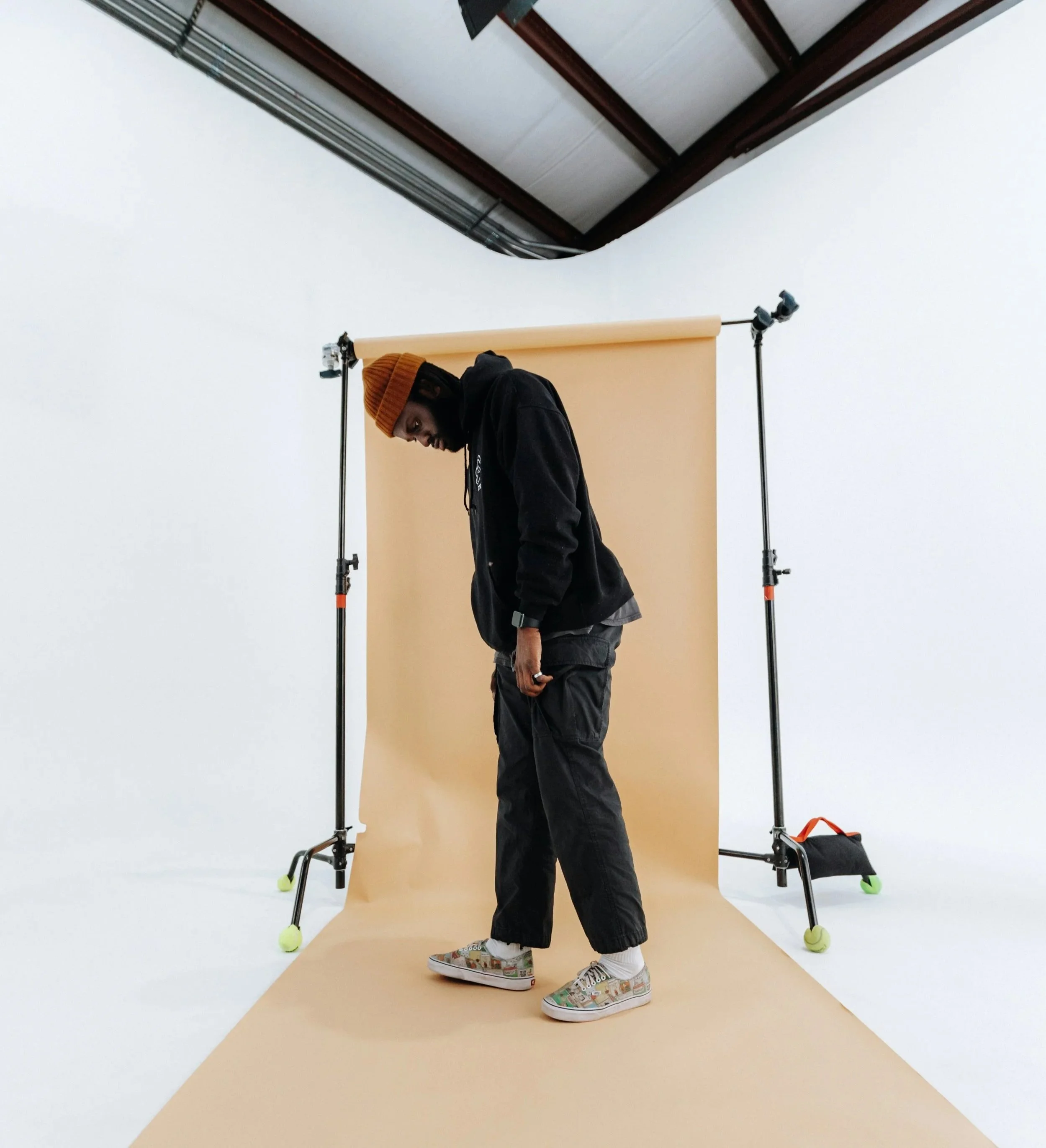 Person standing on a beige backdrop in a photo studio with equipment and white walls.