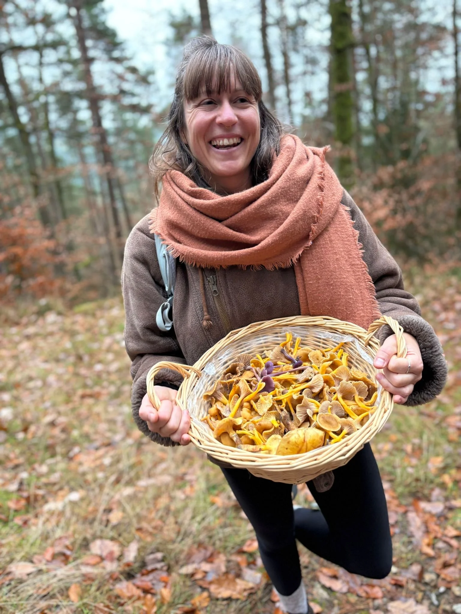 Frau in einem Wald im Herbst hält einen Korb voller Pilze, die sie gesammelt hat.