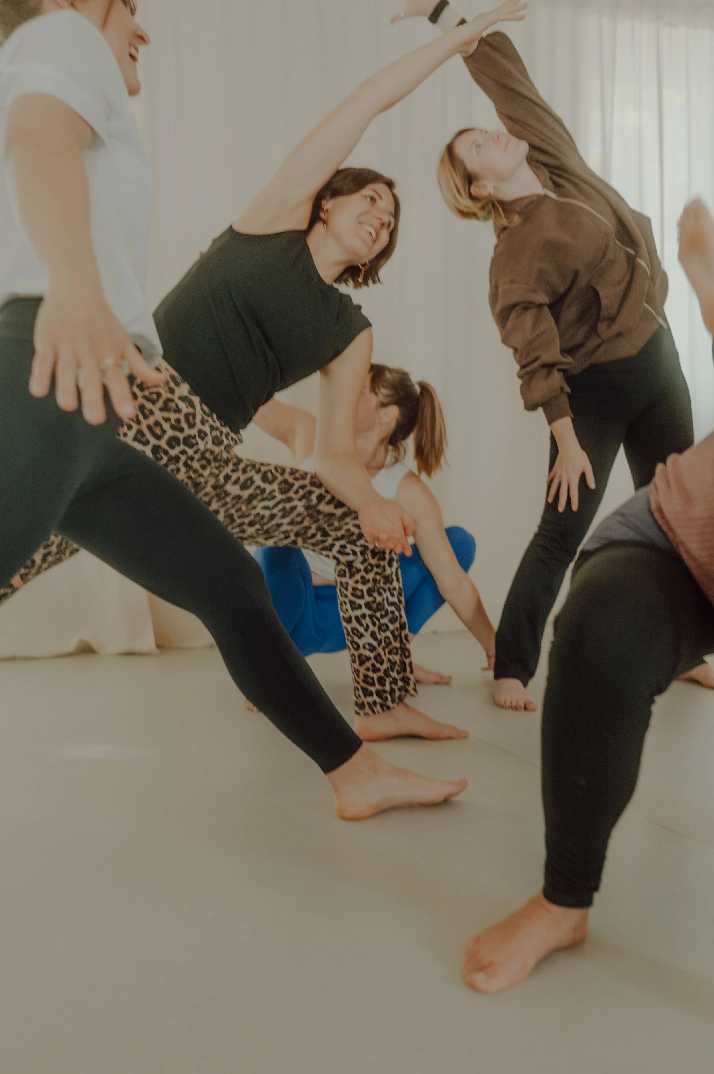 Menschen, die im Yoga-Kurs üben, in einer Reihe auf einem weichen Boden, während sie verschiedene Asanas ausführen, mit natürlichem Licht durch Fenster im Hintergrund.