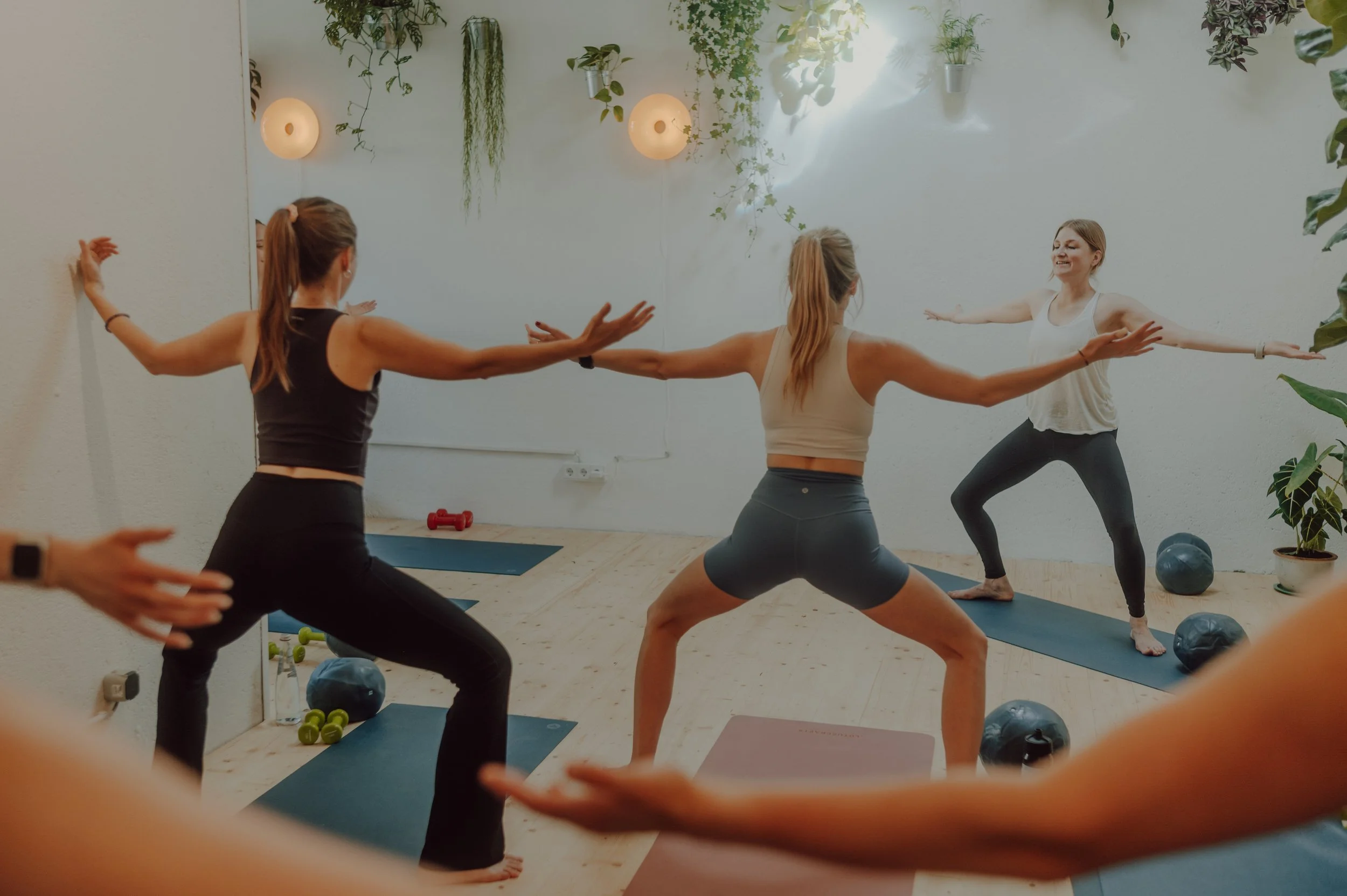 Frauen, die Yoga in einem hellen, mit Pflanzen dekorierten Raum praktizieren.