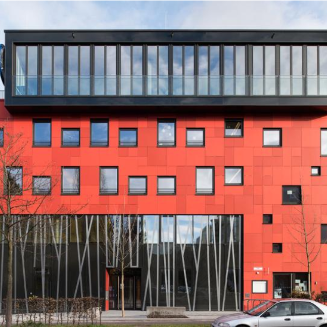 Modernes Gebäude mit roter Fassade, gestreiften Fenstern, Glasbalkon und Verkehrsmittel davor
