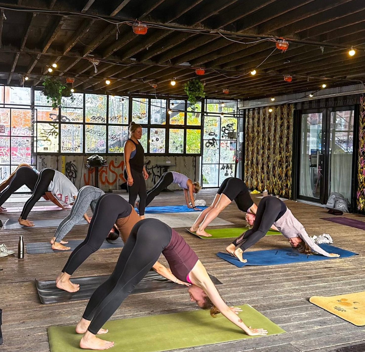 Menschen machen Yoga in einem Raum mit graffiti-verdruckten Wänden und großen Fenstern