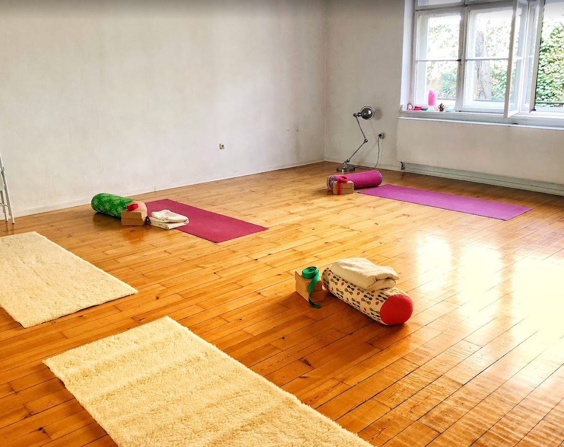 Ein leerer Raum mit Holzfußboden, vorbereitet für eine Yoga- oder Pilates-Klasse, mit Yoga-Matten, Rollen, Handtüchern und Licht von einem Fenster.
