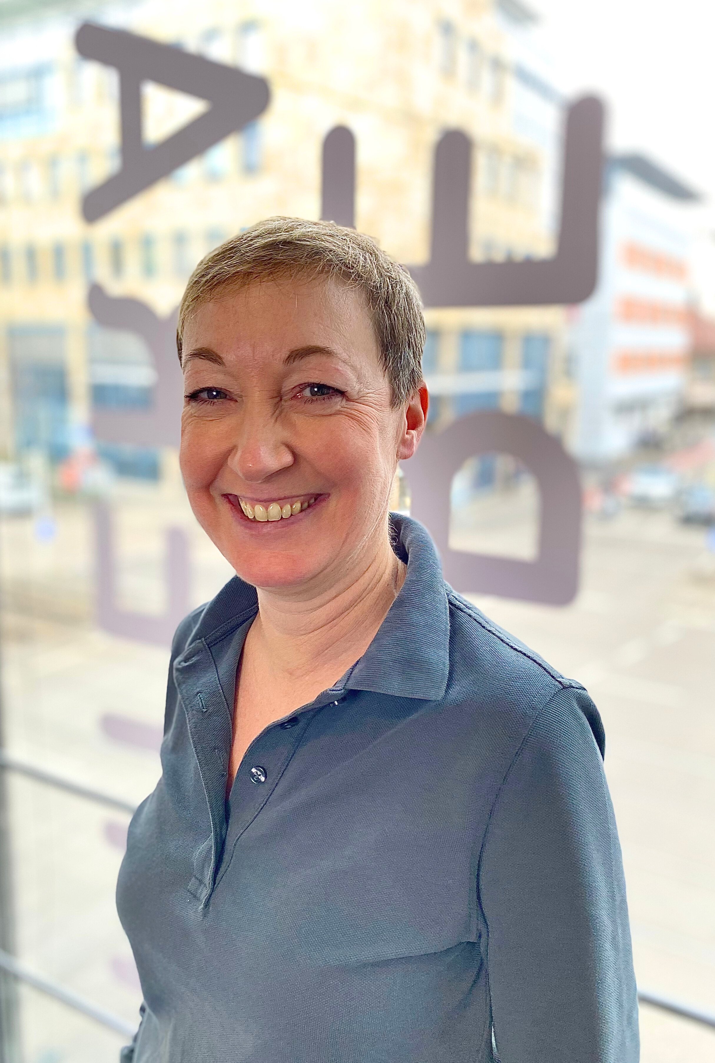 Lächelnde Frau vor einem Fenster mit Graffiti im Hintergrund.