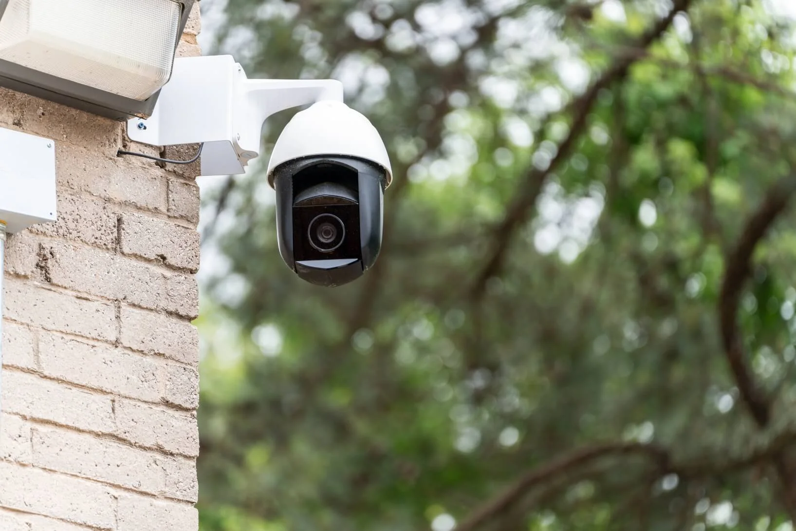 Security camera installed on a brick wall with trees in the background.