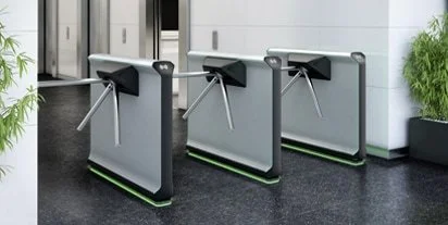 Three modern turnstiles in an office or building entrance, with a leafy green plant nearby.