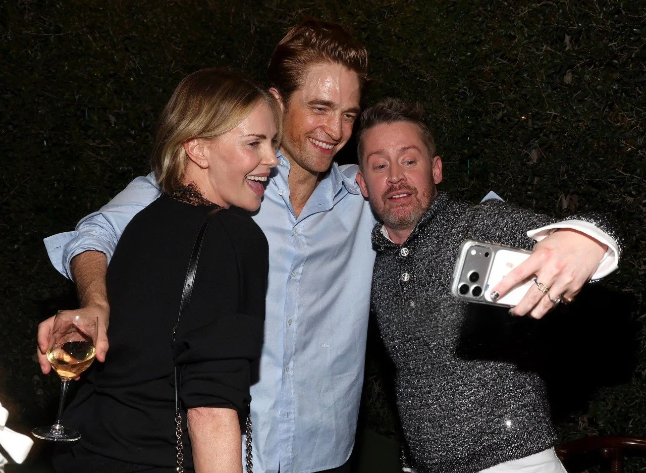 Three people taking a selfie together at an outdoor gathering, smiling and holding drinks.