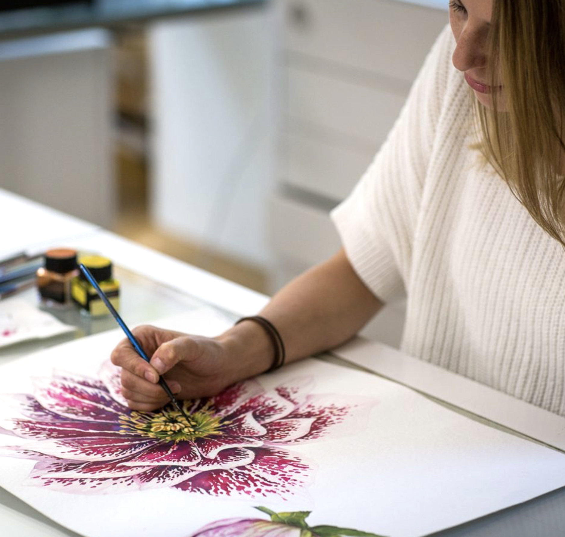 Daniela Binder painting a large, detailed floral design with watercolor paints. This is one element of many for a silk scarf design.