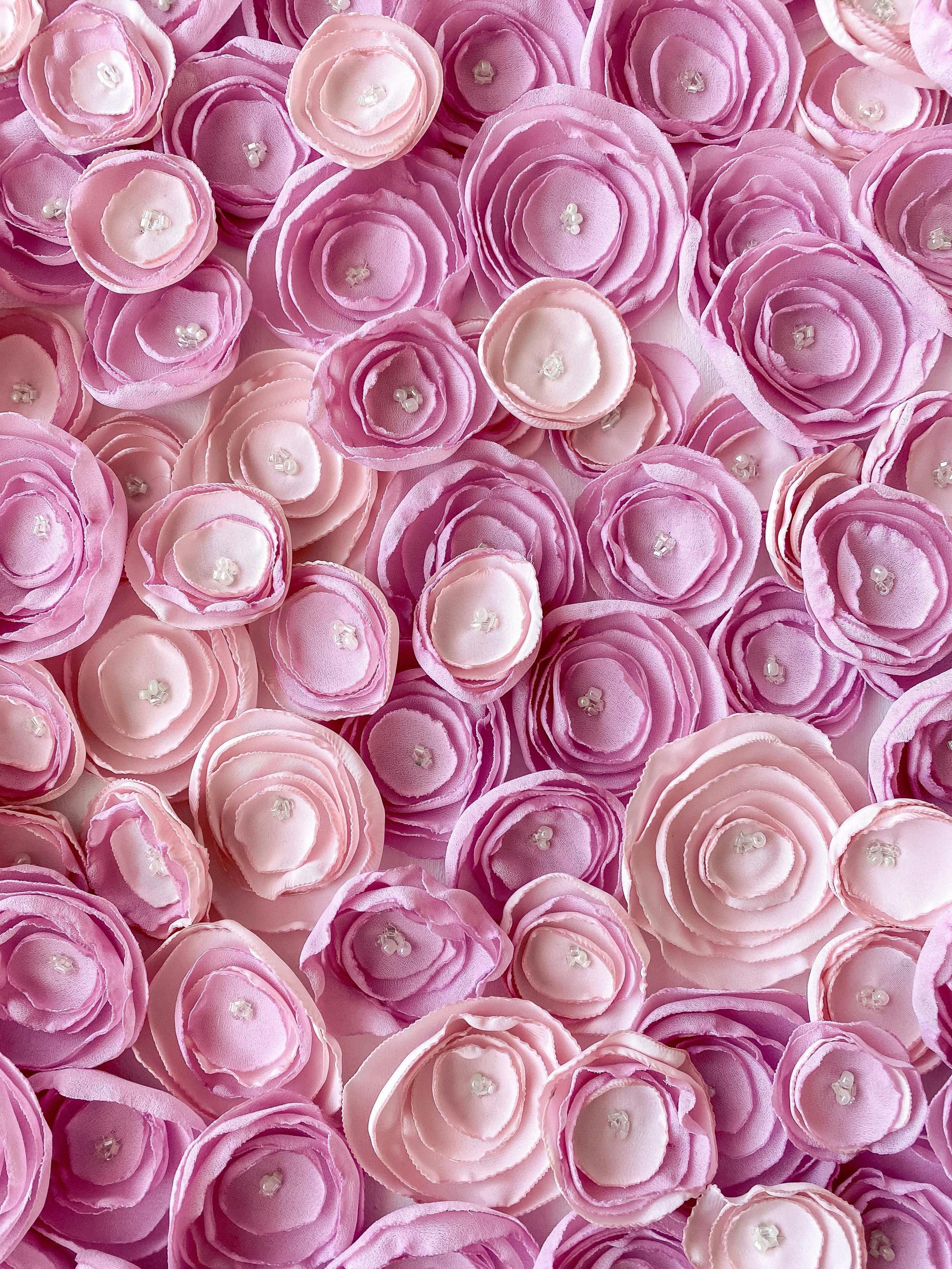 A collection of artificial pink and purple roses with pearl centers layered closely together.