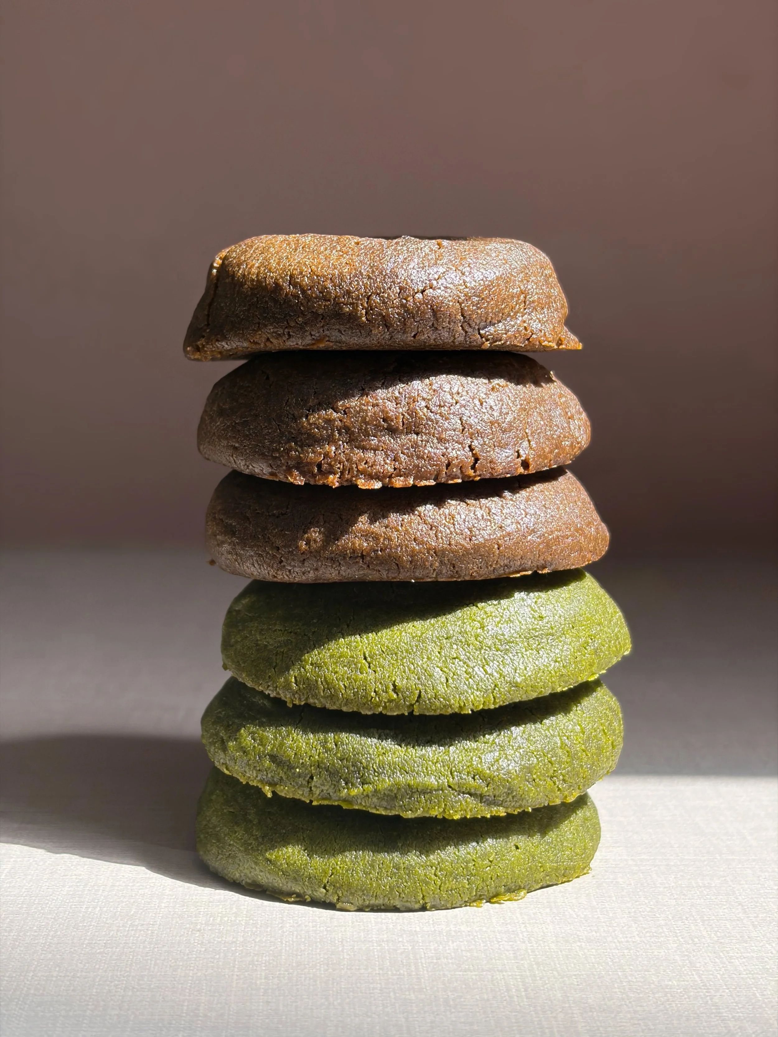 Stacked green matcha-flavored cookies and brown chocolate cookies, sunlight, plain background.