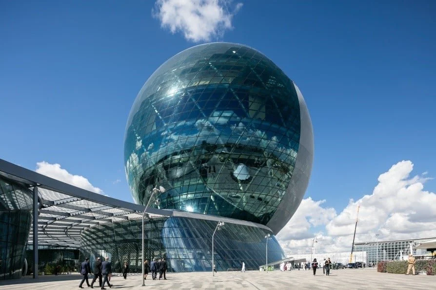 Modernes, kugelförmiges Gebäude mit spiegelnder Glasfassade, umgeben von Menschen im Freien bei sonnigem Wetter.