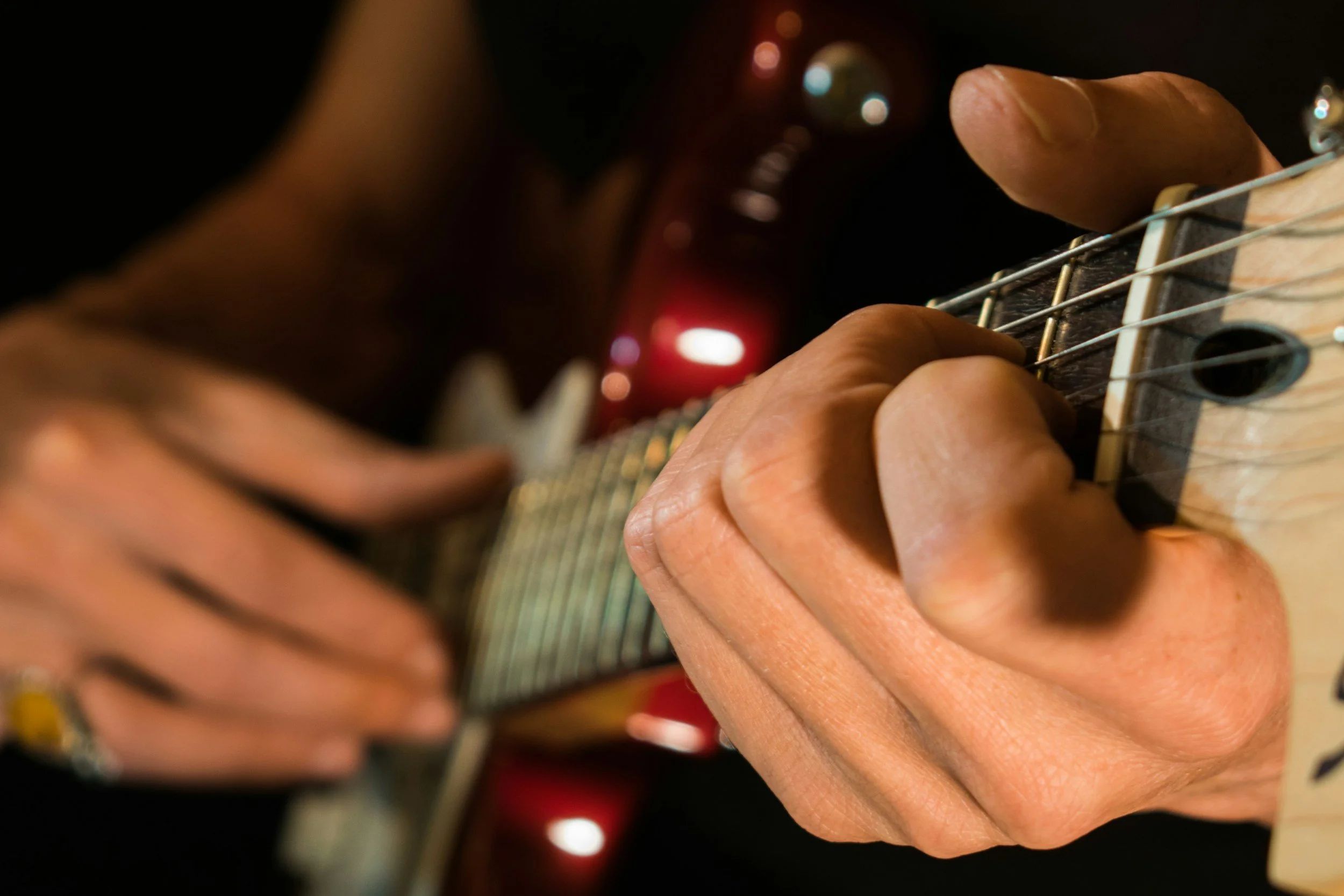 Close-up of a person's hand pressing guitar strings on the fretboard, with focus on the fingers and part of the guitar neck visible.