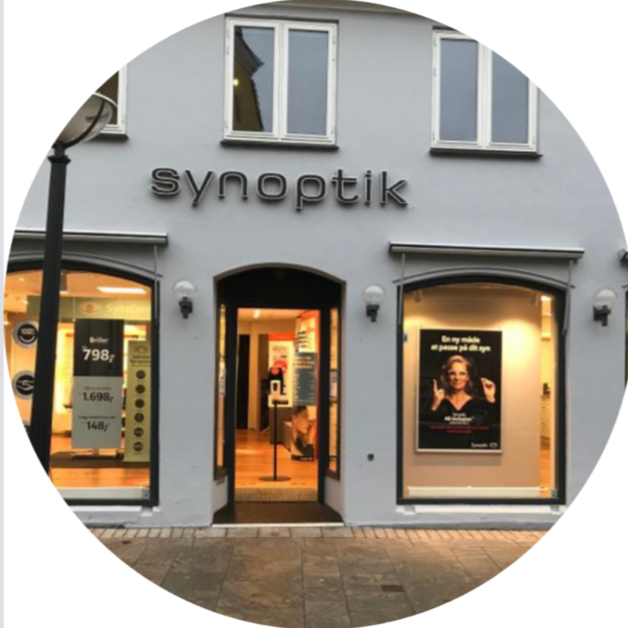 Exterior of a store named 'Synoptik' with large display windows and an entrance door, inside visible promotional posters and lighting.