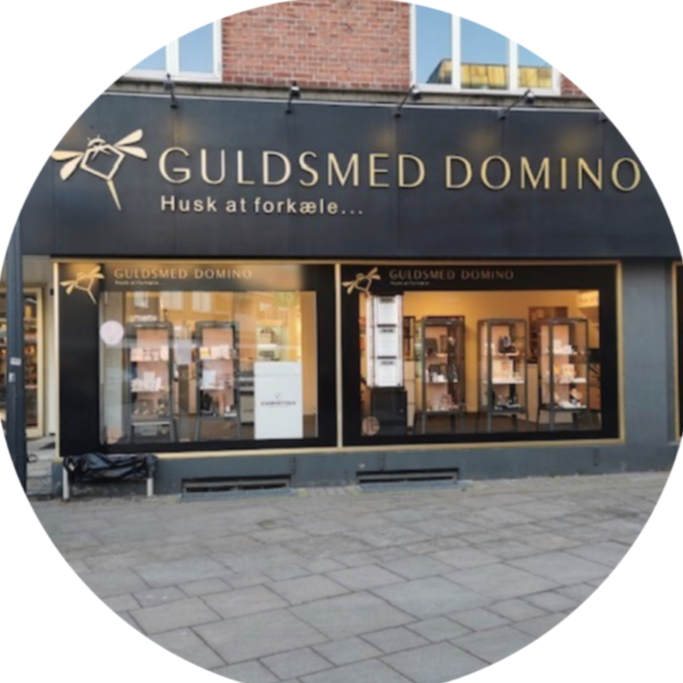 storefront of GULDSED DOMINO jewelry store with large windows and gold lettering, situated on a city sidewalk, featuring jewelry displays inside.