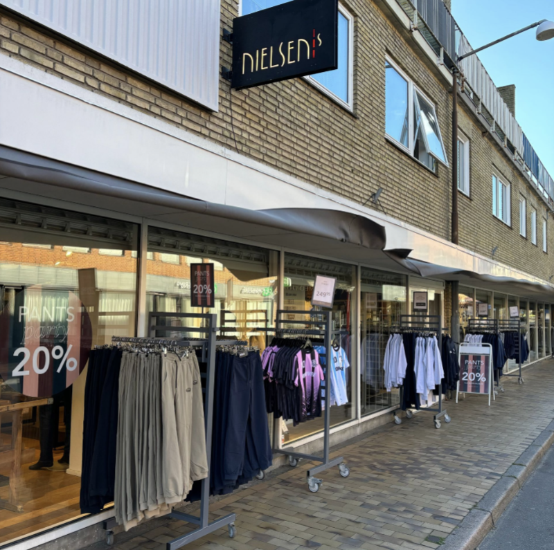 Storefront of Dielsens with clothing racks displaying discounts, in a city street