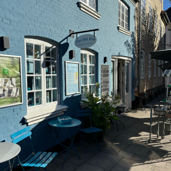 Blue painted building with white-framed windows, outdoor seating with blue chairs and tables, and a sign that reads 'Det Blå Hus'.