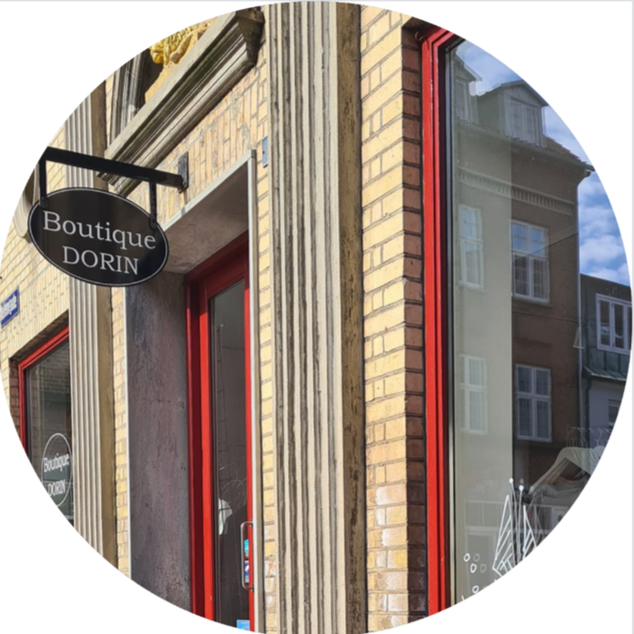 Close-up of a boutique storefront with a black and white sign that reads 'Boutique DORIN', red door, and large reflection windows showing neighboring buildings.
