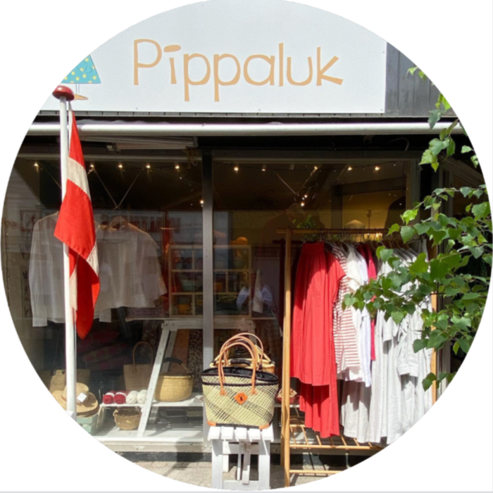 Clothing store named 'Pippaluk' with red and white clothing on display outside, Danish flag, and green foliage.