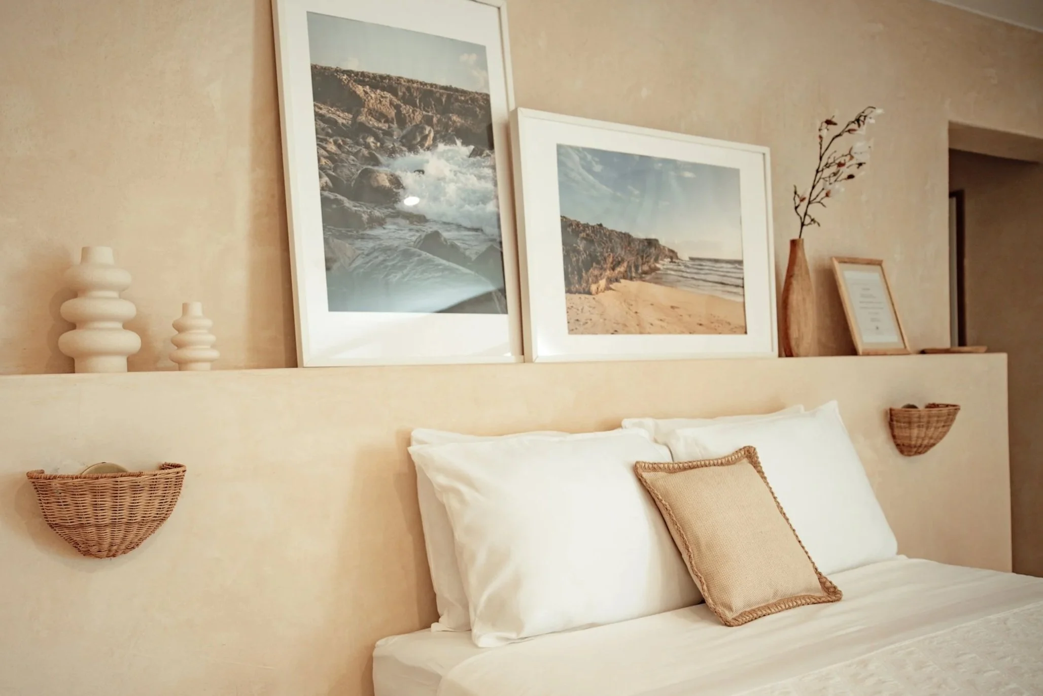 Decorative bedroom with framed landscape photos, white bed pillows, a beige pillow, wooden vases, and wall-mounted woven baskets.