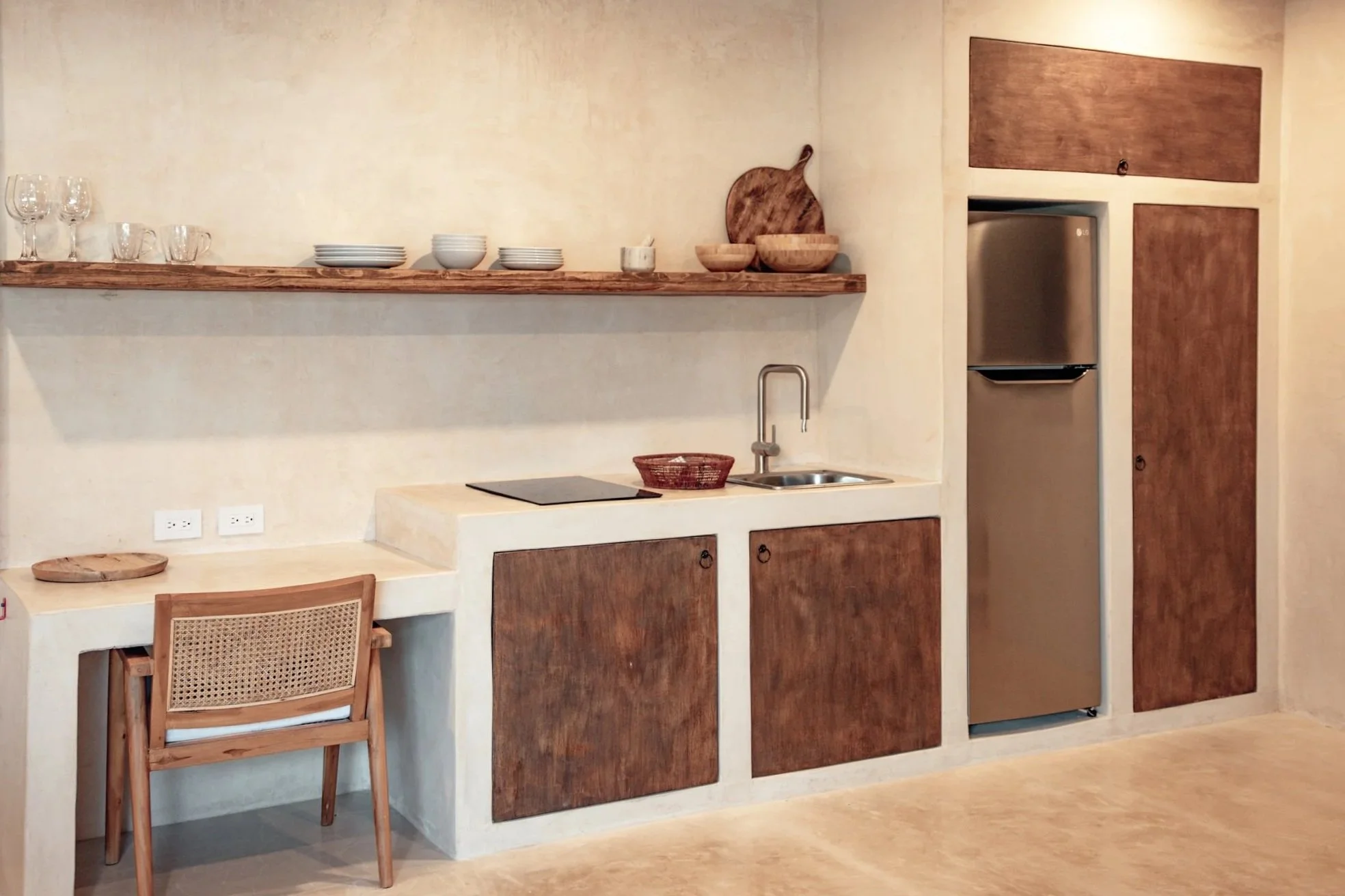 Minimalist kitchen with wooden cabinets, a small sink, a refrigerator, and a floating wooden shelf with dishes and bowls.