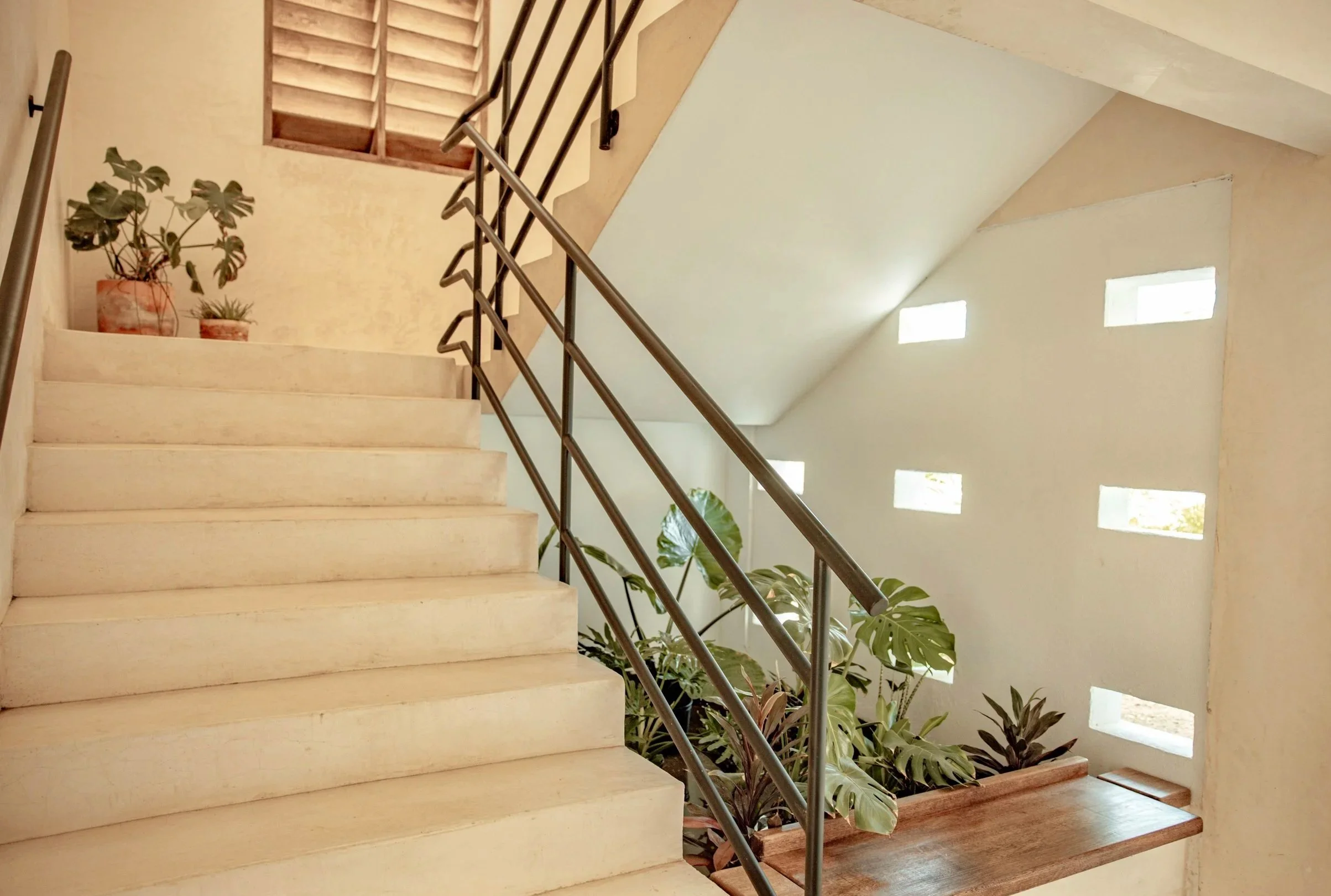 Interior staircase with wooden steps, metal handrails, and potted plants, with small horizontal windows on the wall.