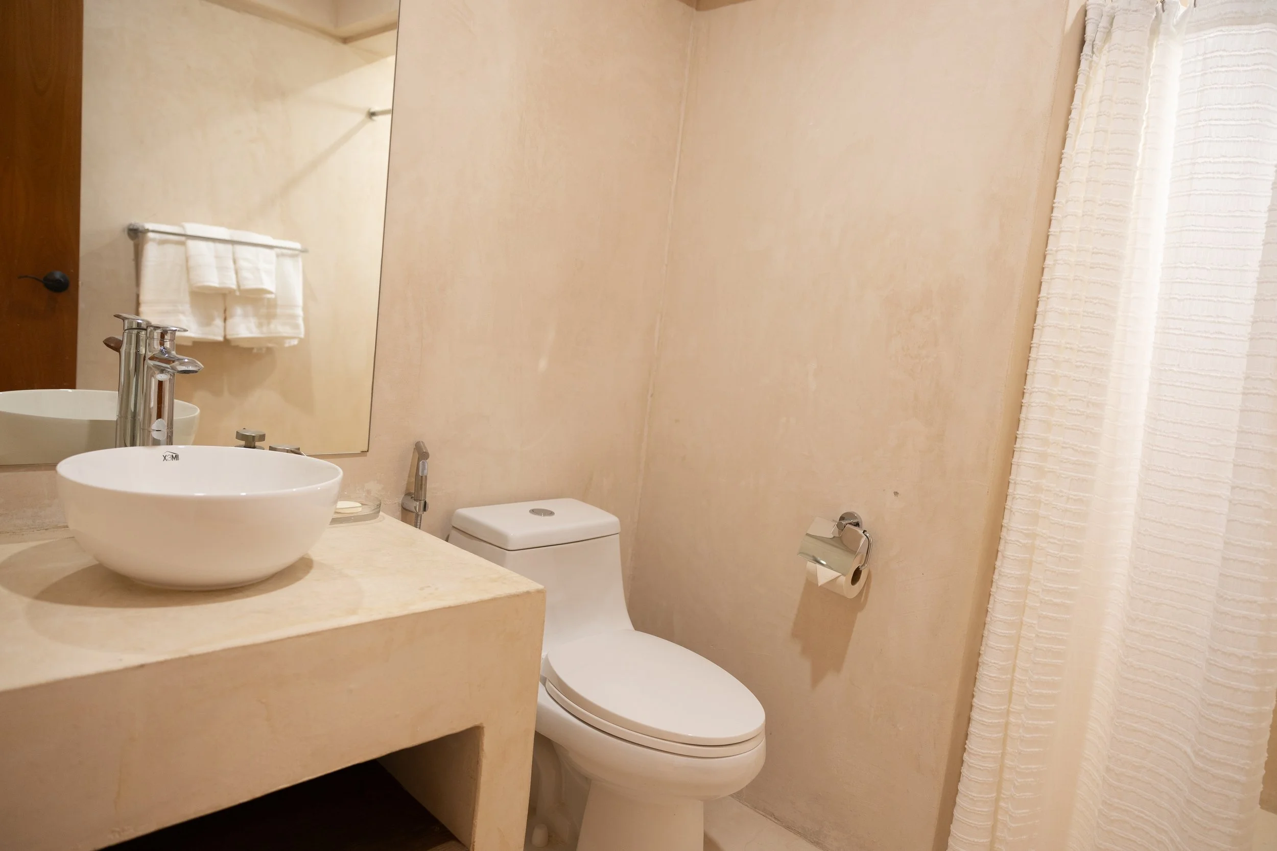 Bathroom with beige walls, a white toilet, a small vanities with a white vessel sink, a silver faucet, large mirror, white towels on towel rack, and a textured shower curtain.