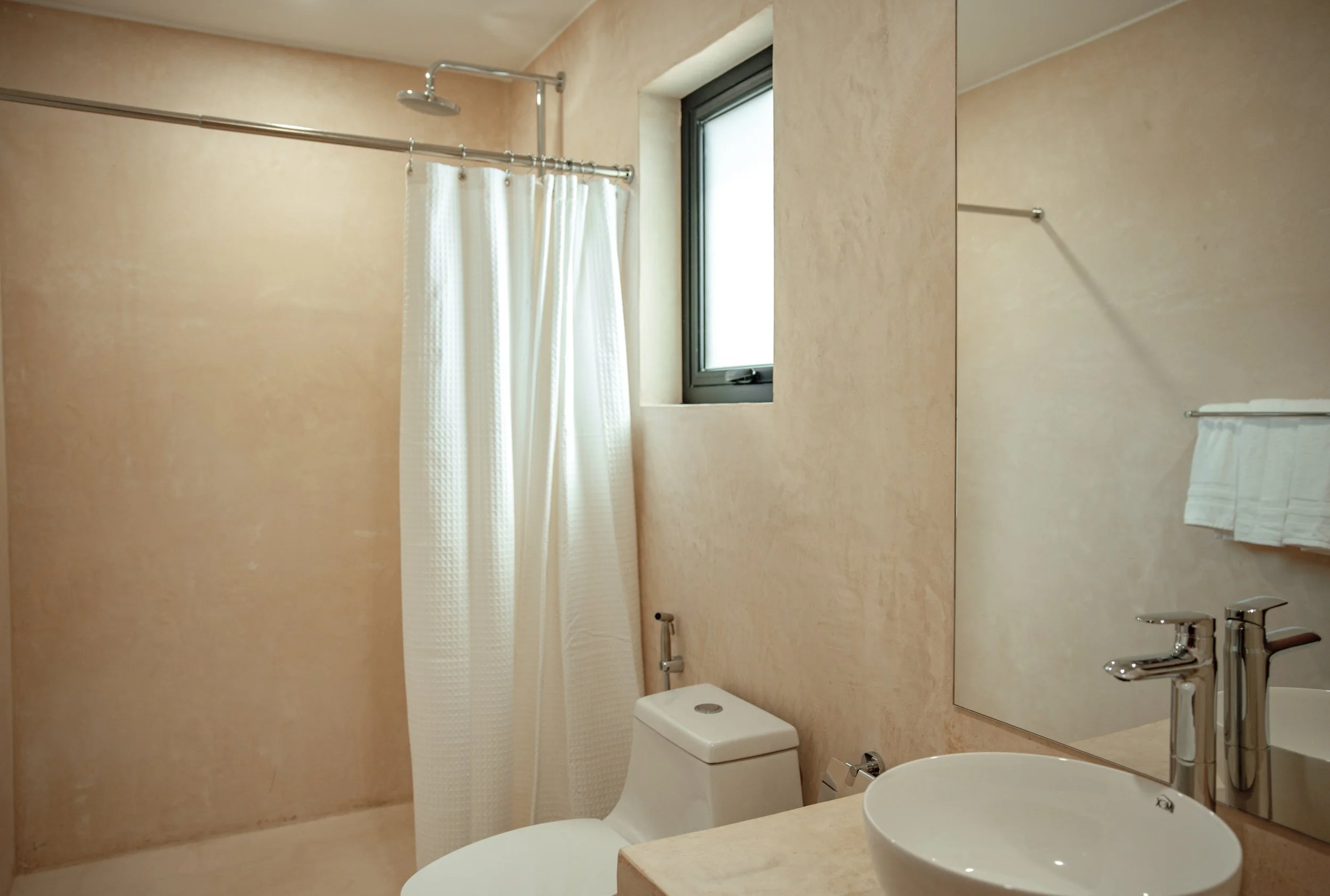 Bathroom with a shower area, a small window, a toilet, a sink with a faucet, and a mirror on the wall.