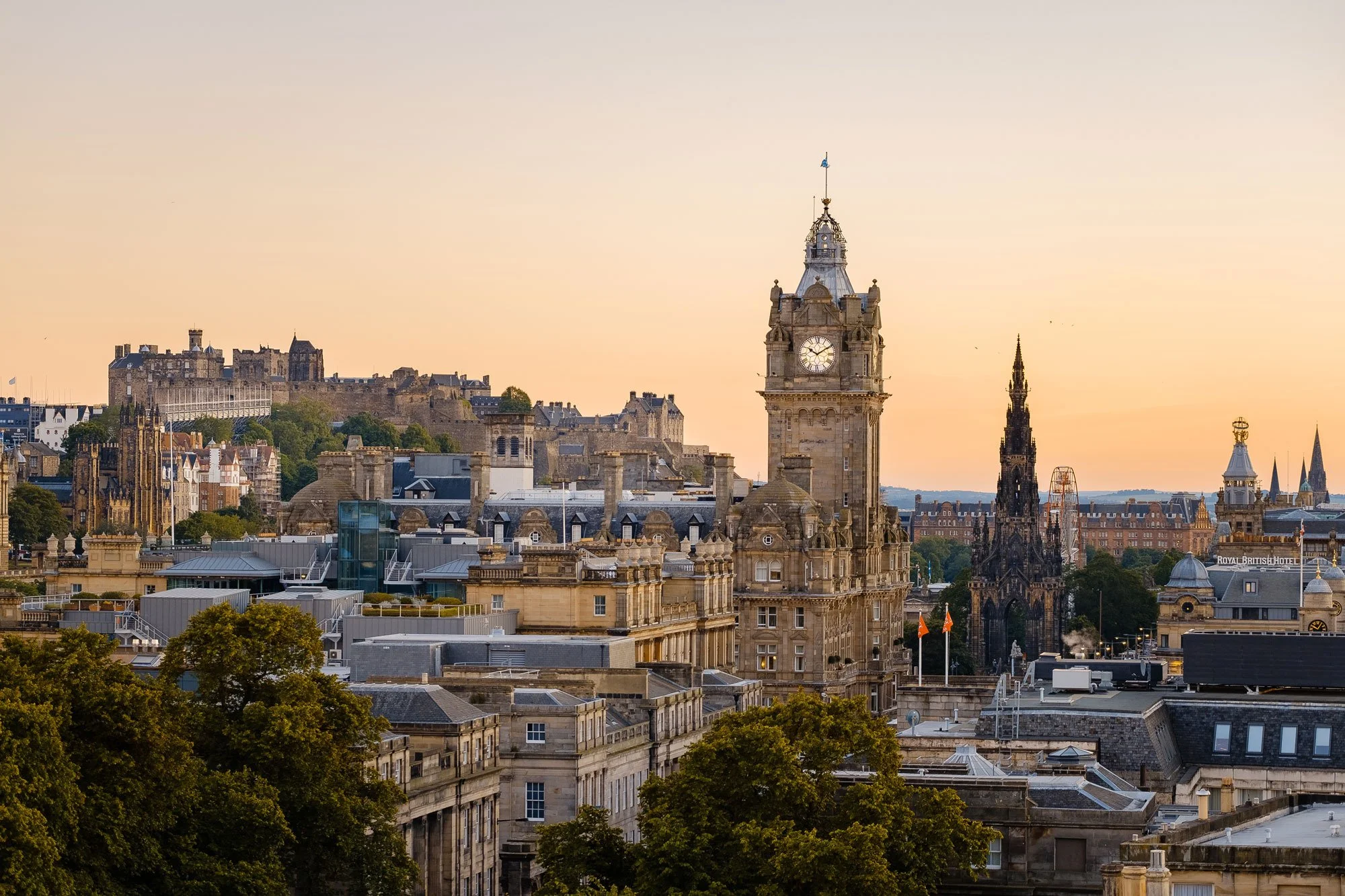 Sunset view of Edinburgh cityscape with historic buildings, including the clock tower and Edinburgh Castle in the background.