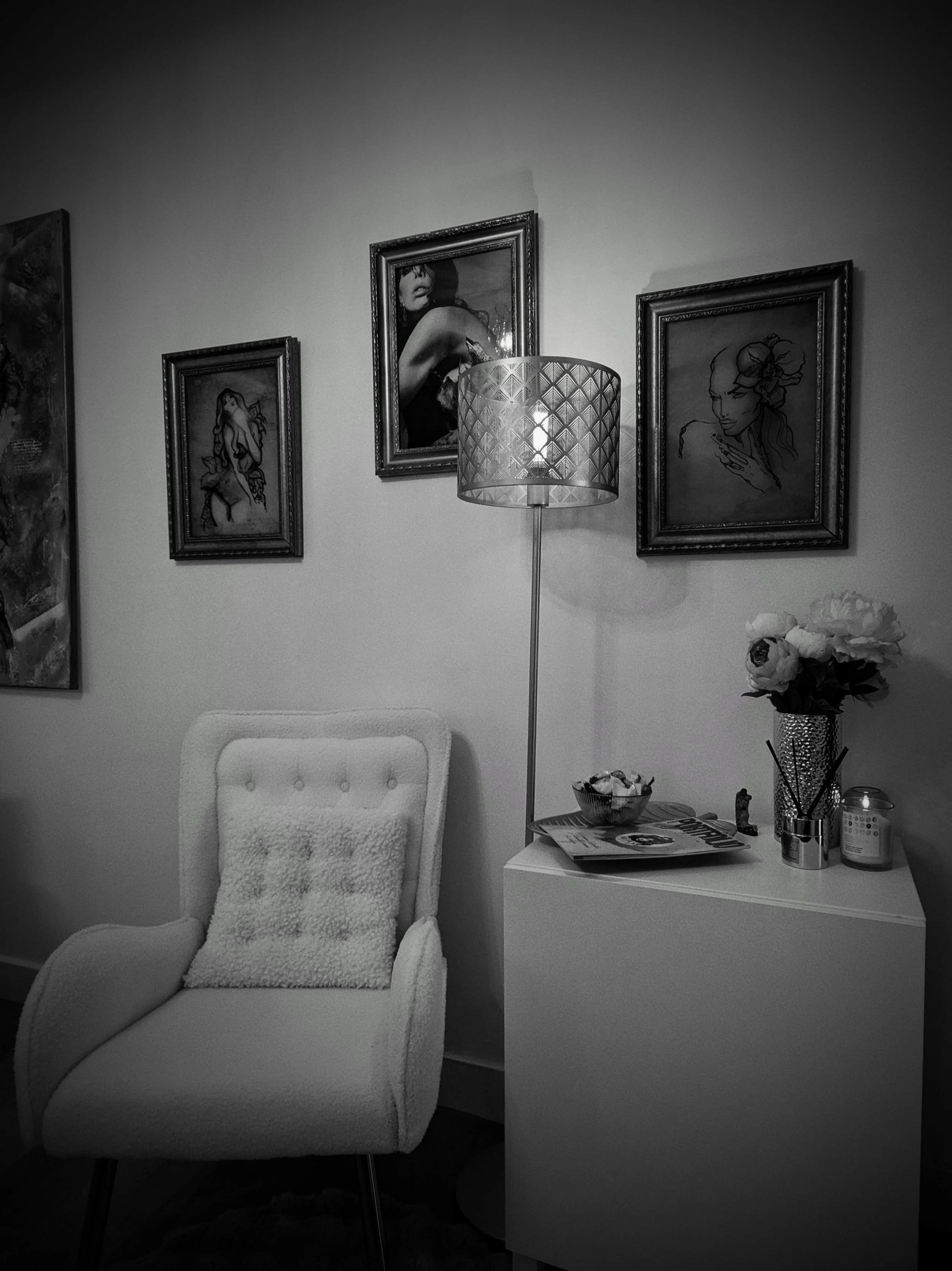Un coin salon en noir et blanc avec une chaise blanche, une lampe sur pied, une table décorative, des plantes en pot, des magazines et des œuvres d'art encadrées suspendues au mur.