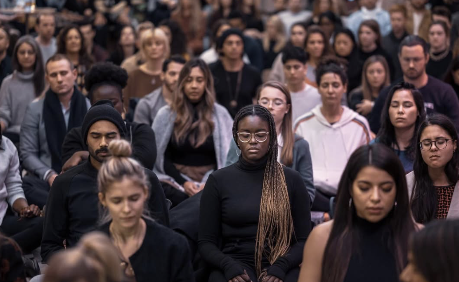 Eine Gruppe von Menschen sitzt im Gebet, ihre Augen geschlossen, in einer ruhigen und meditativen Haltung.