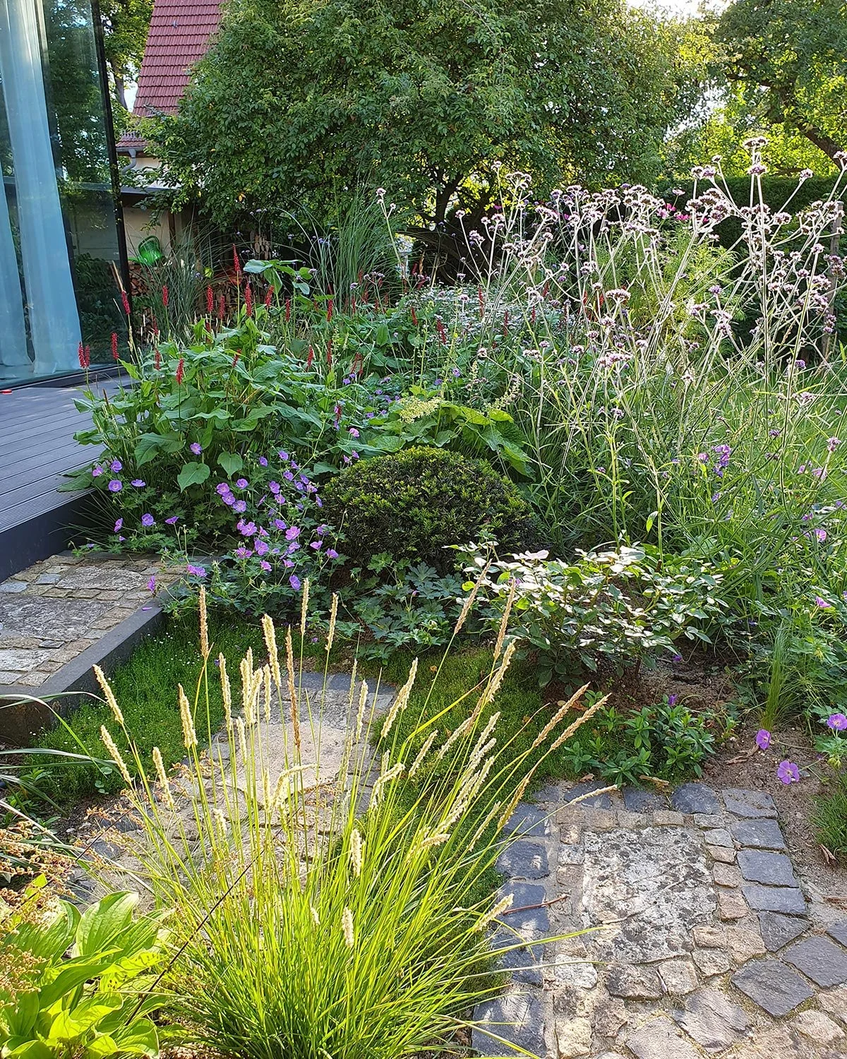 Staudenbeet an Haus und Terrasse mit verschiedenen Pflanzen, neben einem Natursteinweg.