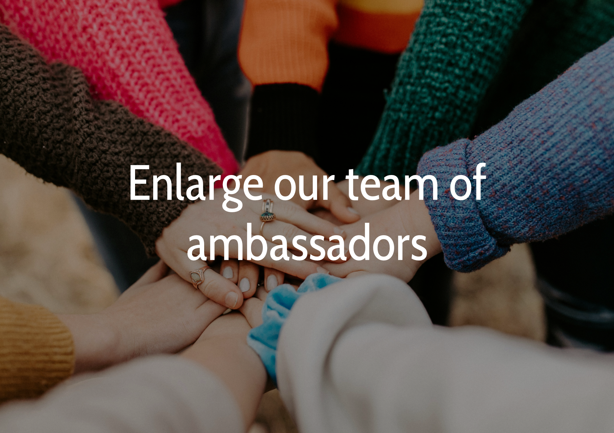 Multiple hands with different skin tones stacked on top of each other, wearing colorful sweaters, symbolizing teamwork and collaboration.