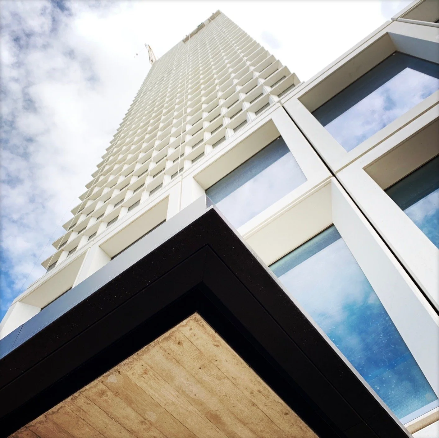 Low-angle view of a modern high-rise building with glass windows and white exterior, set against a partly cloudy sky.