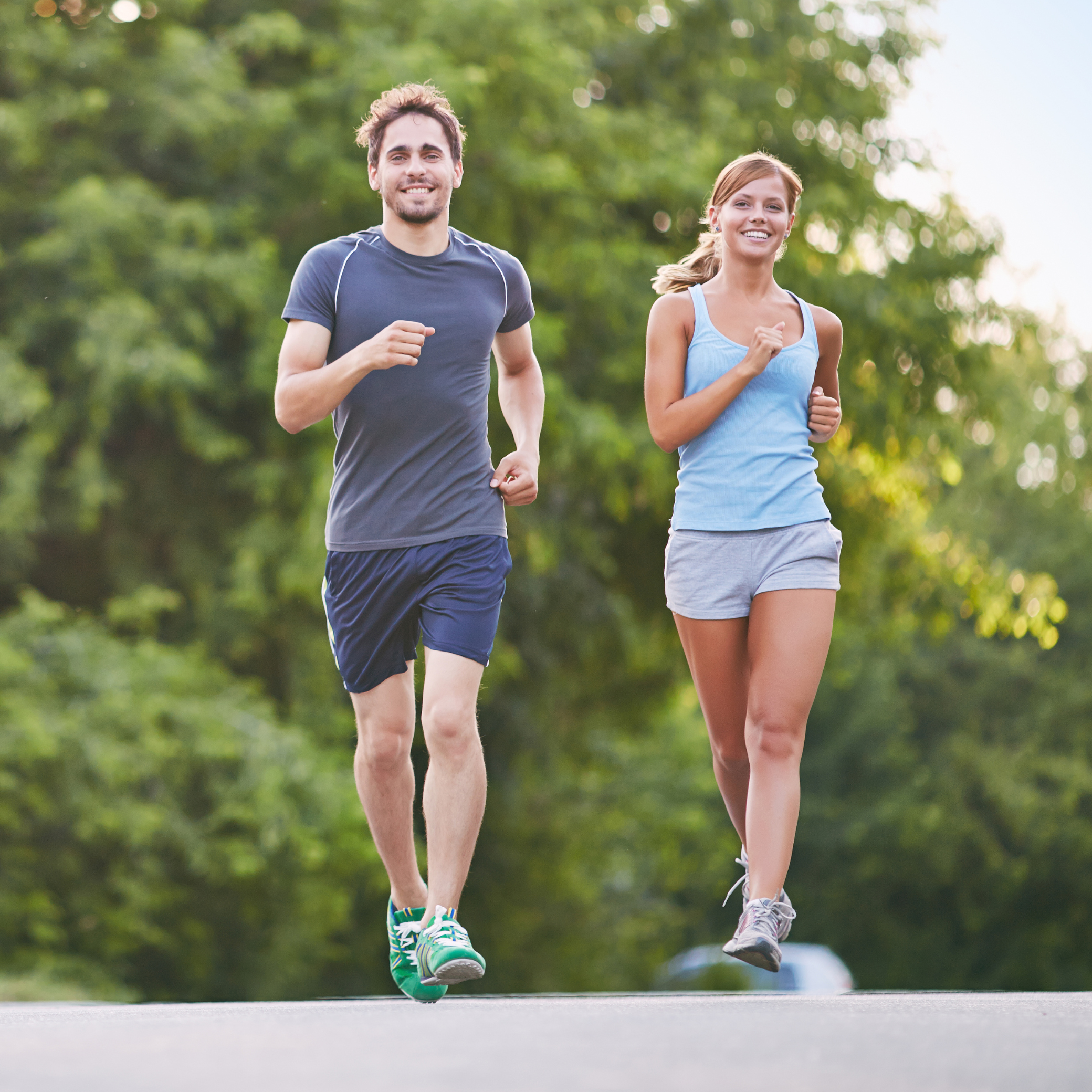 A young man and woman jogging outdoors on a sunny day with green trees in the background.