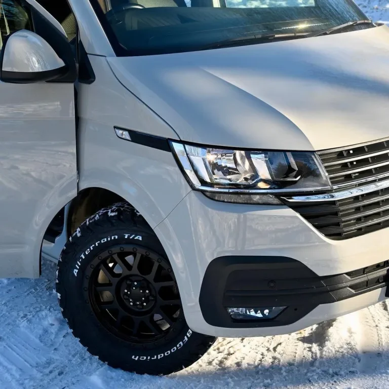 Close-up of the front left side of a white SUV with black tires and snow-covered ground.