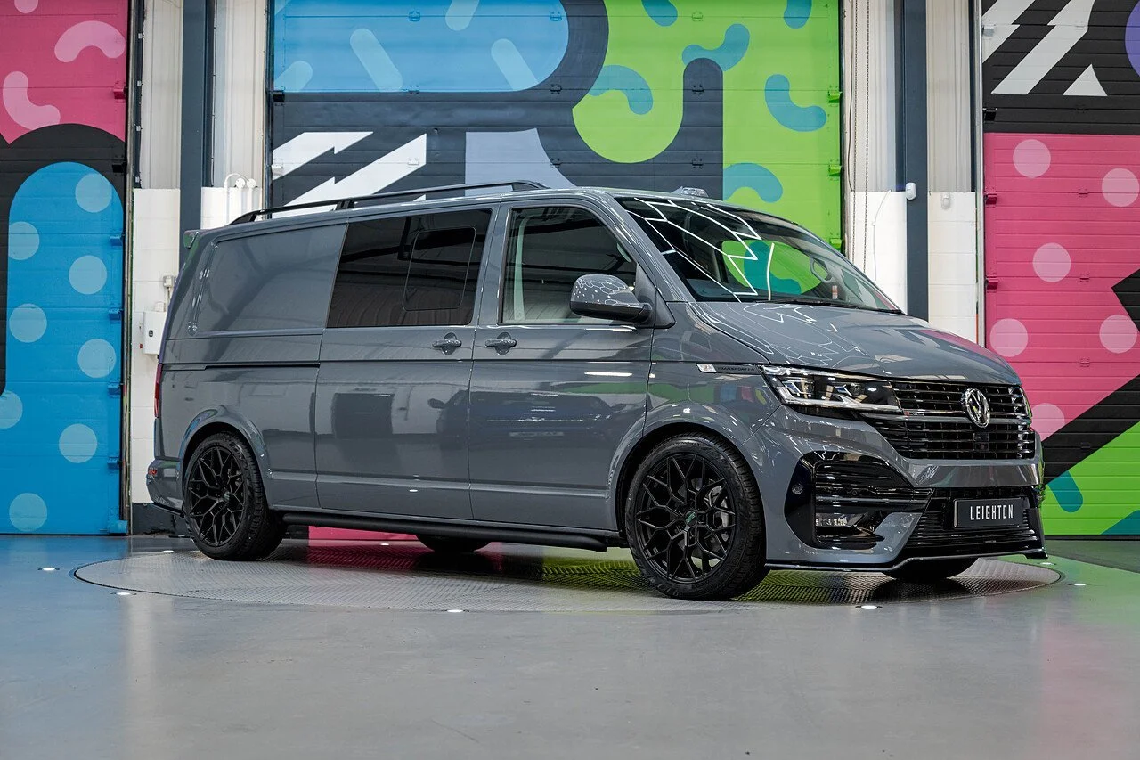 A gray Volkswagen van with black wheels parked inside a colorful, graffiti-style garage.