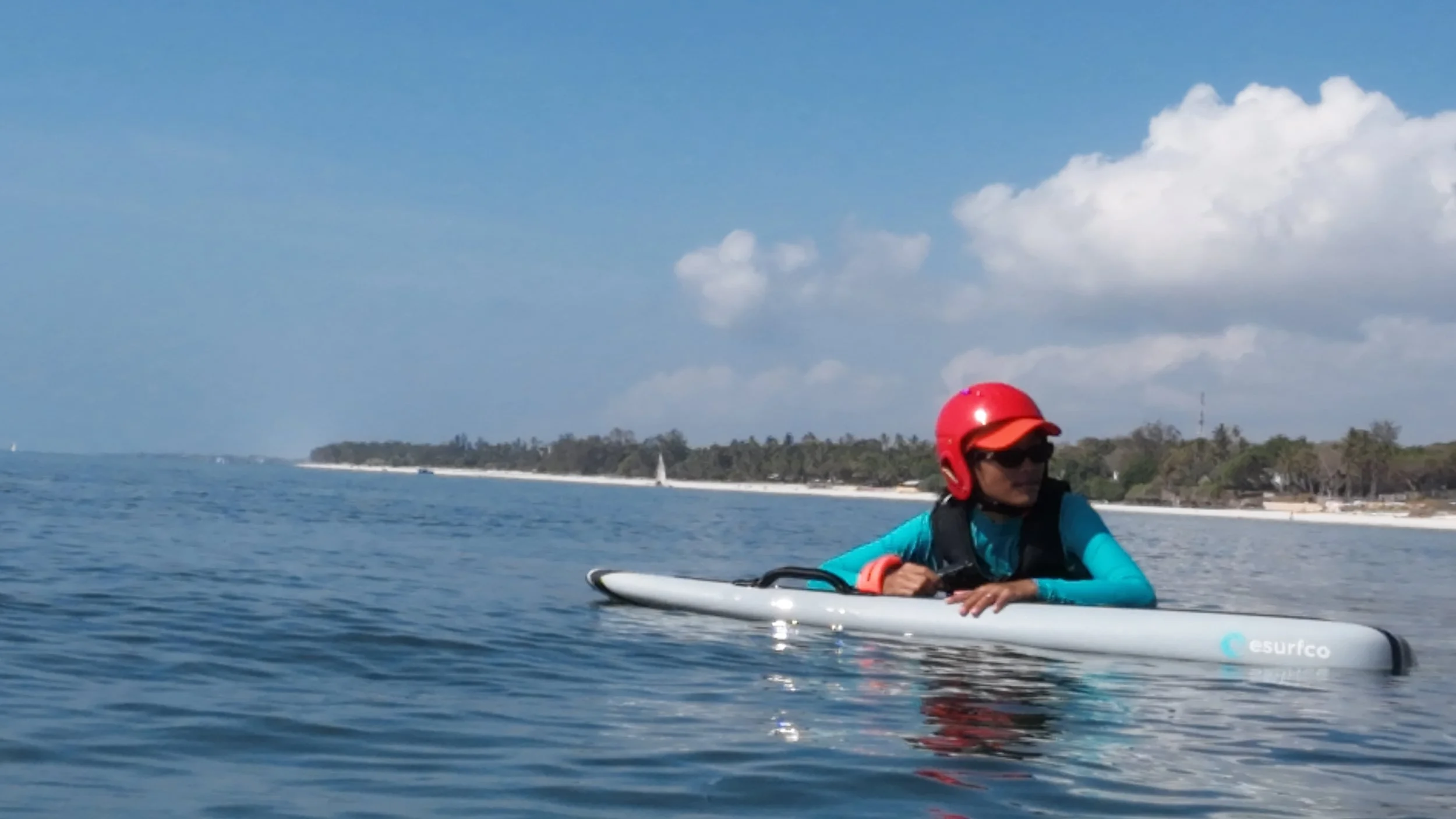 Person in a red helmet and sunglasses lying on paddleboard on calm ocean