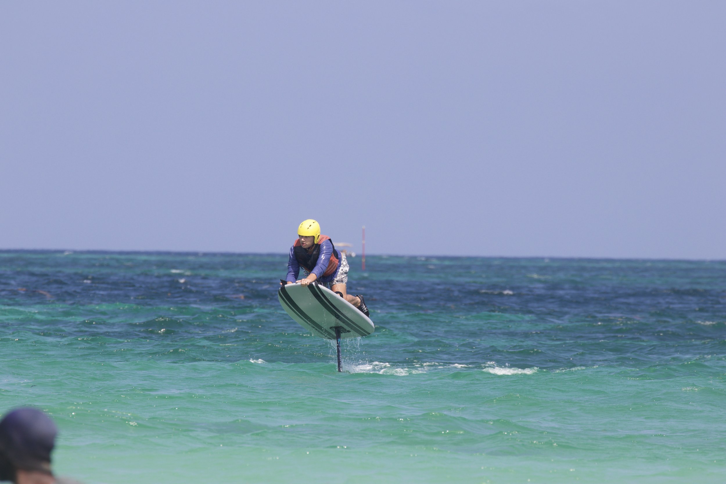 A person in a yellow helmet and life vest is riding a jet-powered surfboard over the ocean waves.