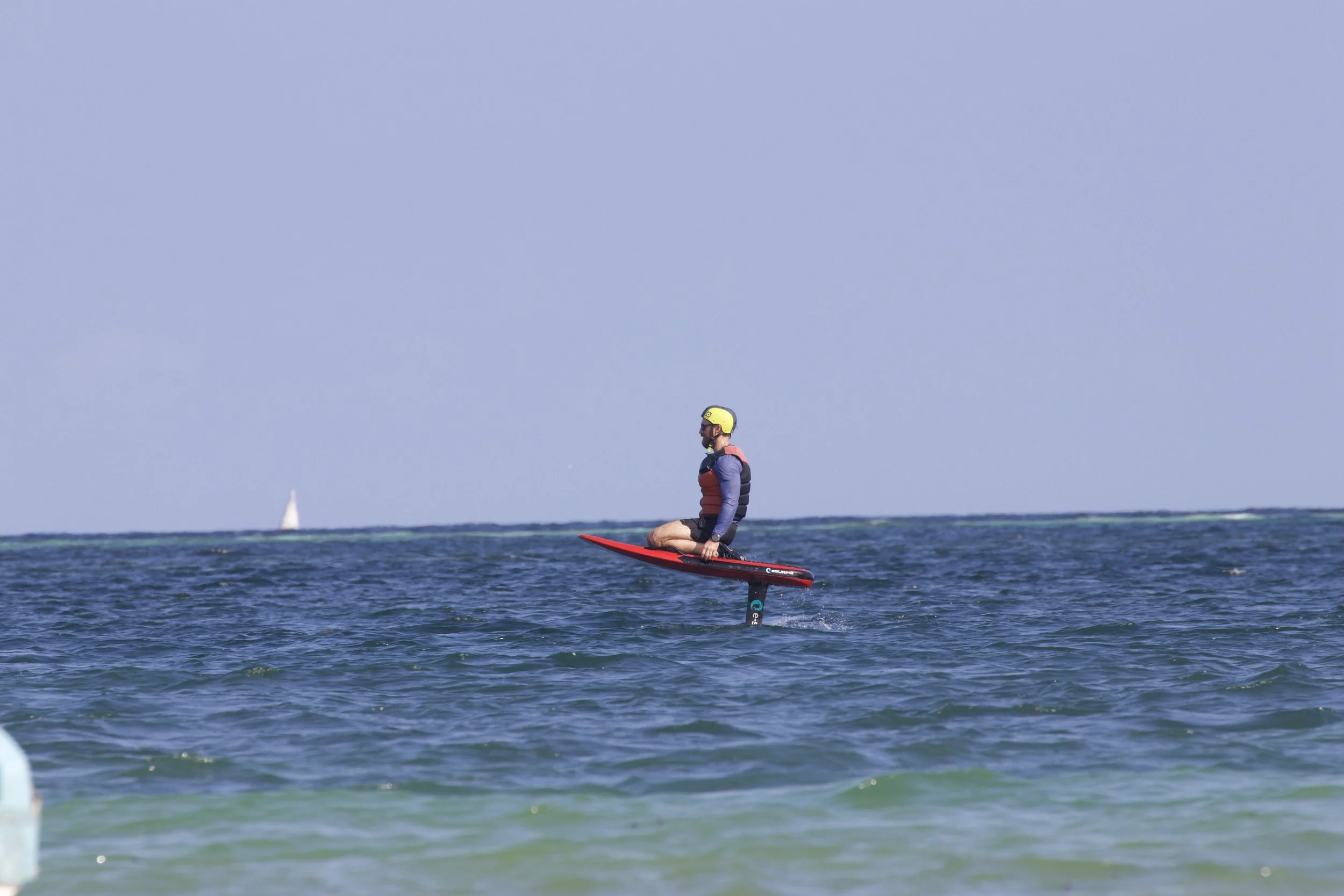 Person riding a jet-powered surfboard on the ocean, wearing a helmet and life jacket.