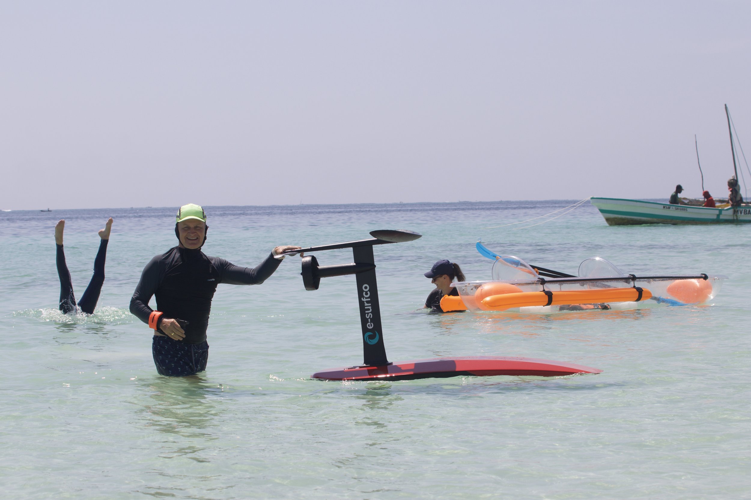 Two people and one person underwater in the ocean with paddleboards, a boat, and a clear sky.