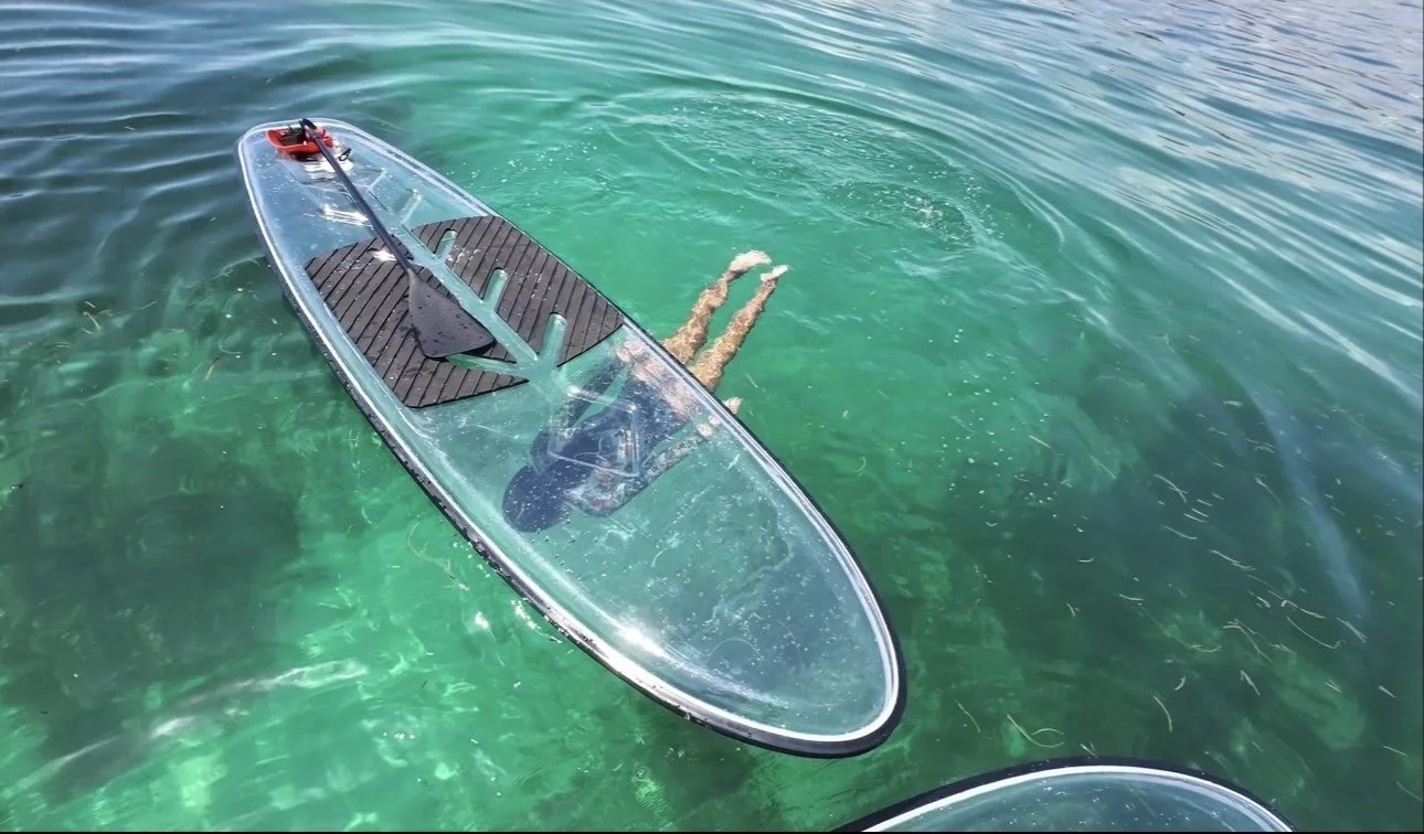 Person floating face down in clear green water near a paddleboard.