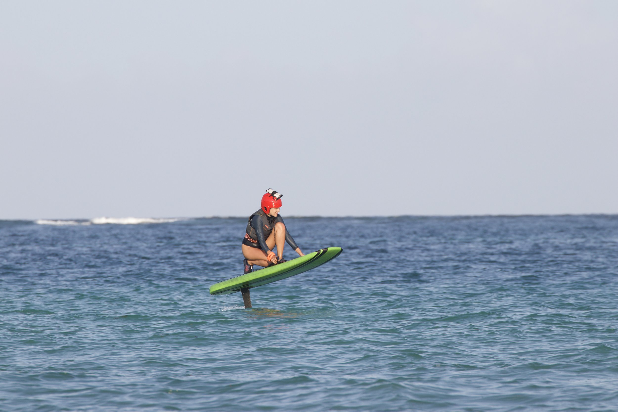 A person wearing a red helmet and a wetsuit is riding a green jet board on the water.