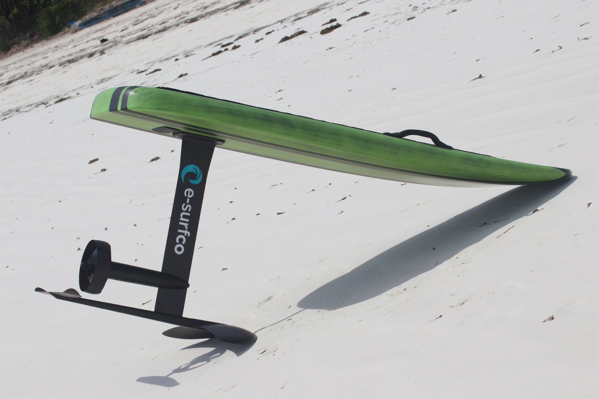 A green and black e-surfGO paddleboard lying on snow with a shadow cast on the snow.